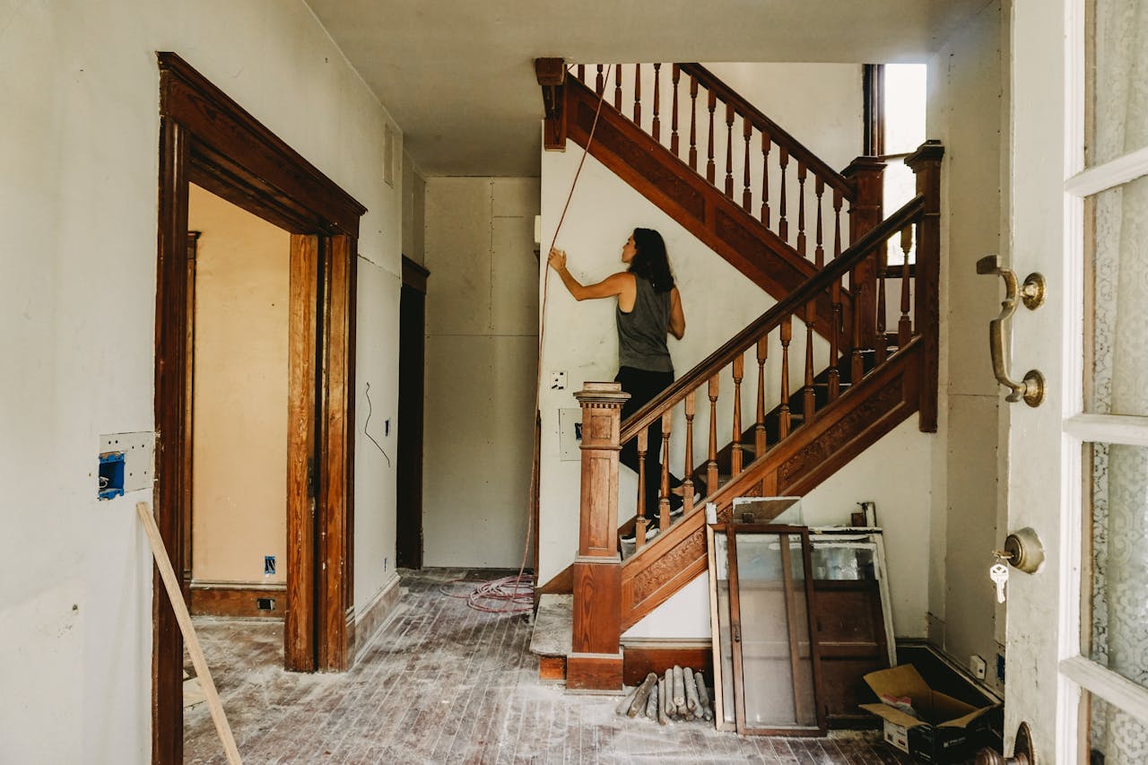 about-us-01 A woman working on home renovation featuring a wooden staircase.